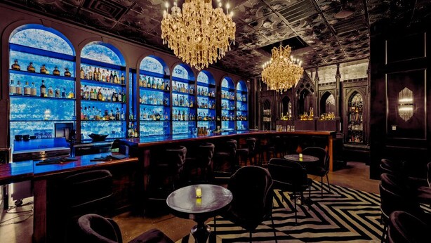 A bar area with multiple shelves of bottles, a chandelier, and a patterned floor. - Inn Cahoots on 6th: 5BR/13Beds - Pool, Rooftop, Garden Bars, Walk to Everything (Austin)