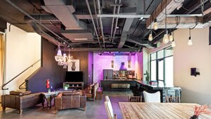 A modern interior with a wooden dining table, leather sofas, and a bar area with a large TV screen. - Inn Cahoots on 6th: 5BR/13Beds - Pool, Rooftop, Garden Bars, Walk to Everything (Austin)
