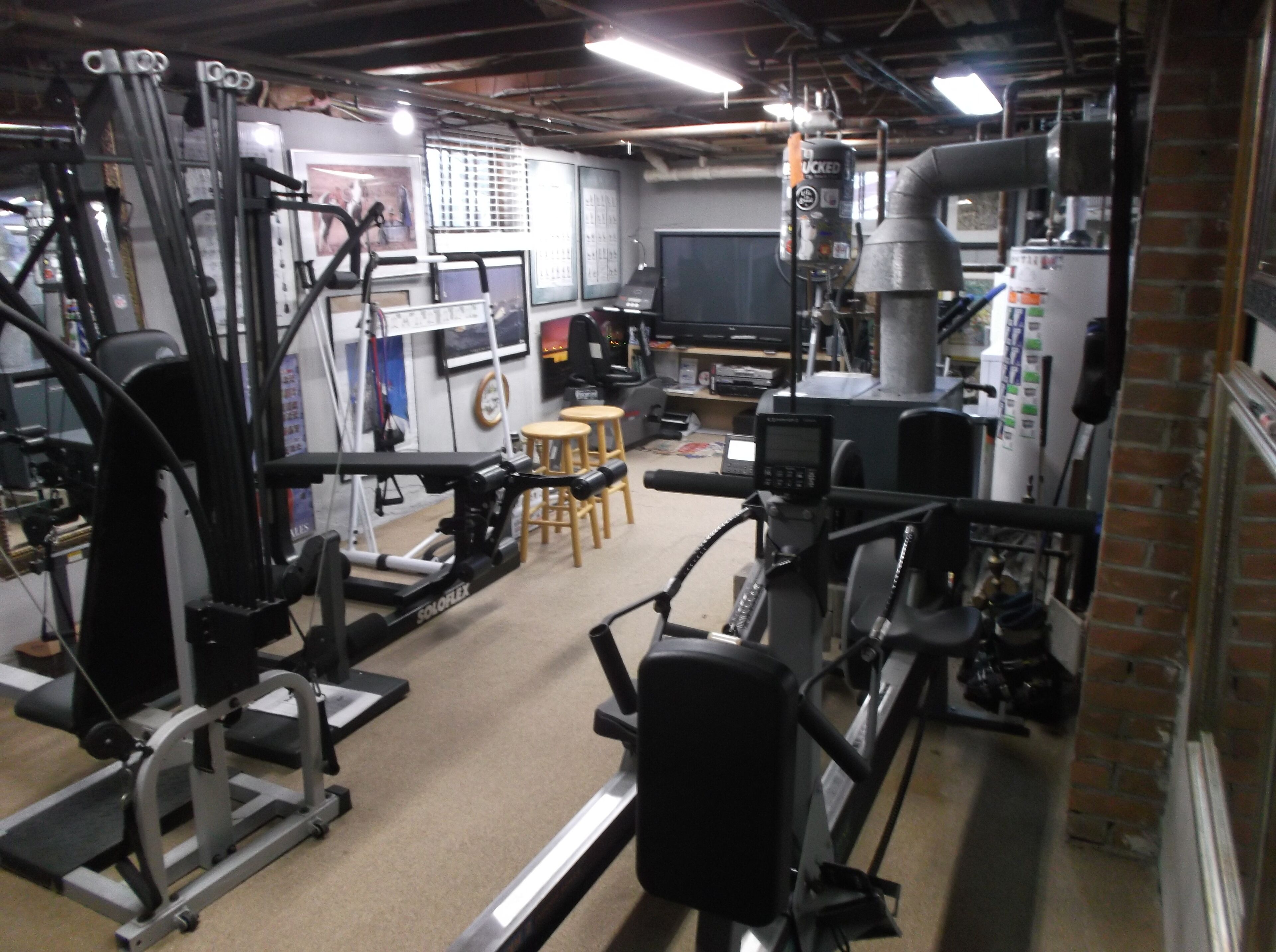 A gym with various exercise equipment, a television, and a brick wall.