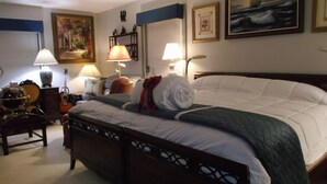 Quarto bem iluminado com uma cama grande, duas mesas de cabeceira, um violão e diversas decorações nas paredes.