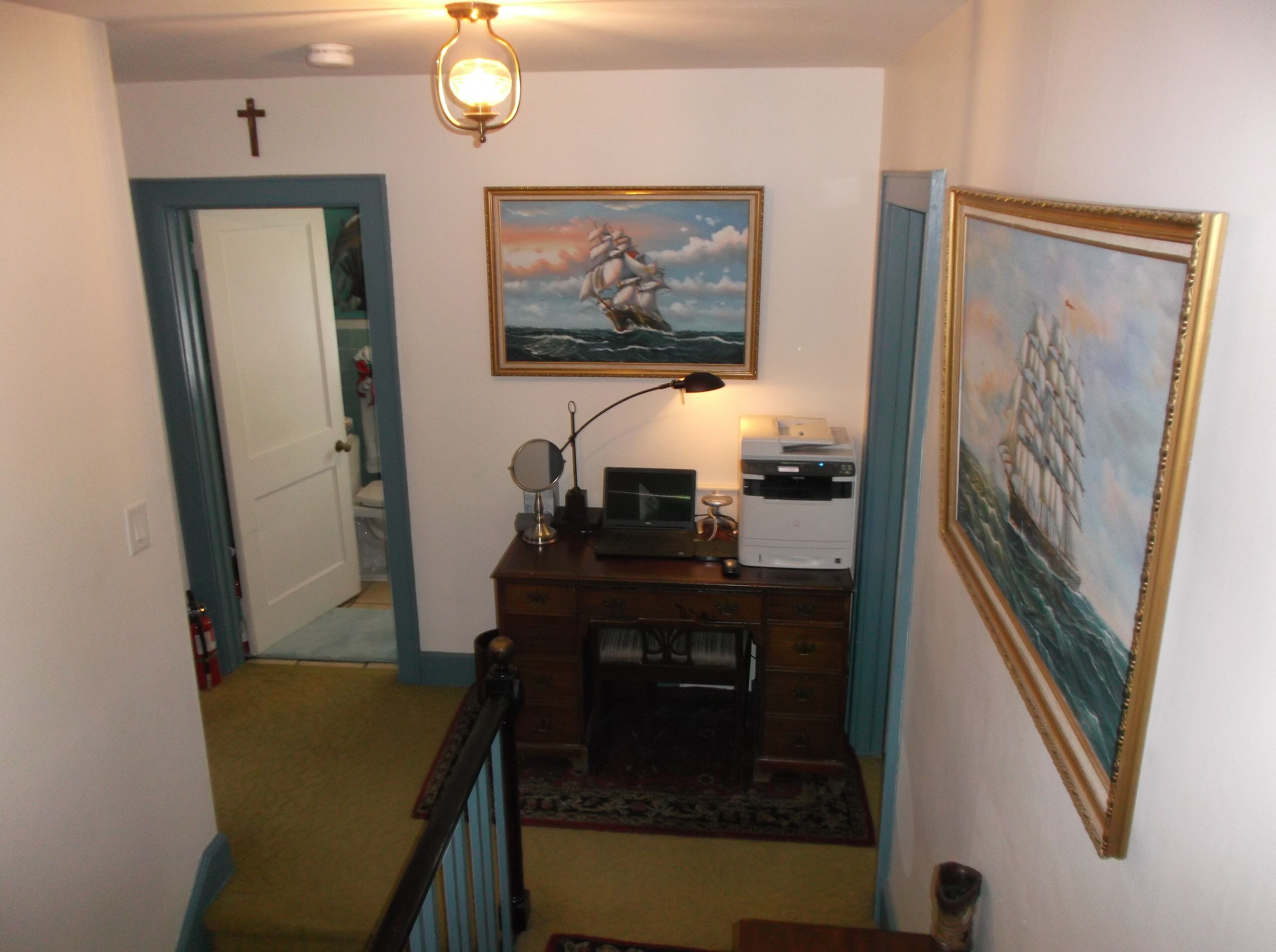 Un couloir avec un bureau, une imprimante et des tableaux encadrés.