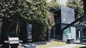 Ein modernes Gebäude mit Glasfassade, Grill und Steinskulpturen in einer angelegten Grünfläche.