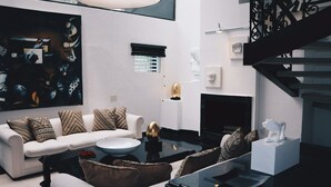 Ein modernes Wohnzimmer mit einem weißen Sofa, gemusterten Kissen, einem Glastisch und einem Kamin.
