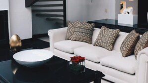 Ein modernes Wohnzimmer mit einem weißen Sofa, gemusterten Kissen, einem schwarzen Couchtisch und einer schwarzen Treppe mit aufwendiger Geländerarbeit.