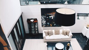 Ein modernes Wohnzimmer mit einem weißen Sofa, gemusterten Kissen, einem schwarzen Couchtisch und einer großen schwarzen Stehlampe.