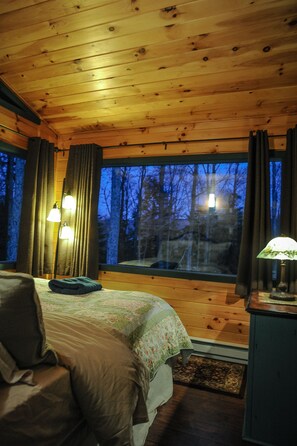 A cozy cabin room with a wooden ceiling, a large window, a bed with a green blanket, and a nightstand with a lamp. - TOP RATED ULTIMATE YEAR ROUND PLAYGROUND (Elka Park)