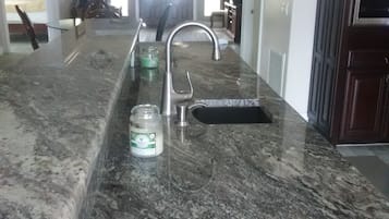A kitchen with a granite countertop, stainless steel sink, and a ceiling fan.
