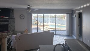 A spacious living room with a large window, a white sofa, a ceiling fan, and a stone fireplace. - Gunter's Paradise Retreat.   Pool paddle boards and kayaks! (Crystal River)