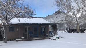 Una pensione con un tetto imbiancato dalla neve, un portico con sedie e una montagna sullo sfondo.