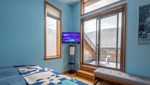 Une chambre à coucher avec un lit, un banc, une télévision et une fenêtre donnant sur un paysage enneigé.