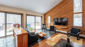 Un salon moderne avec un mur en bois, de grandes fenêtres, un téléviseur à écran plat, un canapé et une table basse.