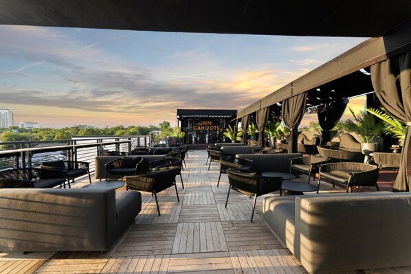 A deck with outdoor seating, a sign for 'Inn Cahoots', and a view of the city skyline.
