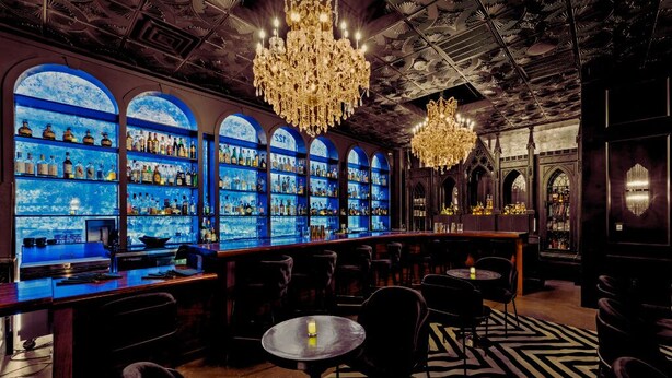 Eine Bar mit blauer Wandbeleuchtung, Kronleuchtern und einem gemusterten Teppich.
