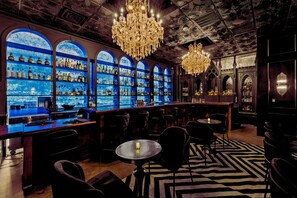 A bar with a blue-lit wall, chandeliers, and a patterned carpet.