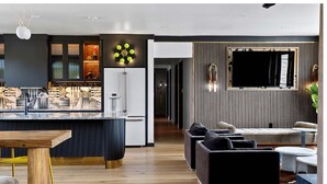 Eine moderne Küche mit einer zentralen Kochinsel, ein Essbereich mit einem Holztisch und ein Wohnzimmer mit Sofa und Fernseher.