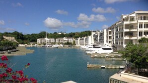 Un port de plaisance où sont amarrés des yachts, un bâtiment au bord de l’eau doté de balcons et un ciel d’un bleu limpide.