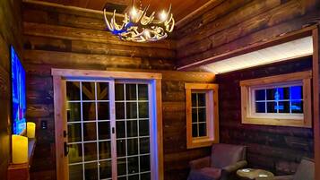 A log cabin interior with a chandelier, wooden walls, a sliding glass door, and a patterned rug.