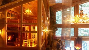 Un intérieur de chalet chaleureux avec une cheminée, des murs en bois et une grande fenêtre.