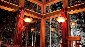 Un intérieur de chalet chaleureux, doté d’une grande fenêtre, d’une cheminée et d’un lustre original.
