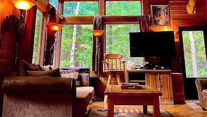 L’intérieur chaleureux d’un chalet, avec un grand plafond en bois, un lustre, un téléviseur et une tête de cerf accrochée au mur.