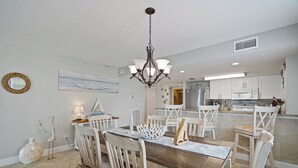 Un coin repas avec une table et des chaises en bois, un lustre et une cuisine en arrière-plan.