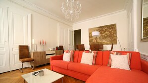 A living room with a red sofa, a white coffee table, and a chandelier. - 3 bedrooms Premium Apartment - La Suite Lanterne (Lyon)