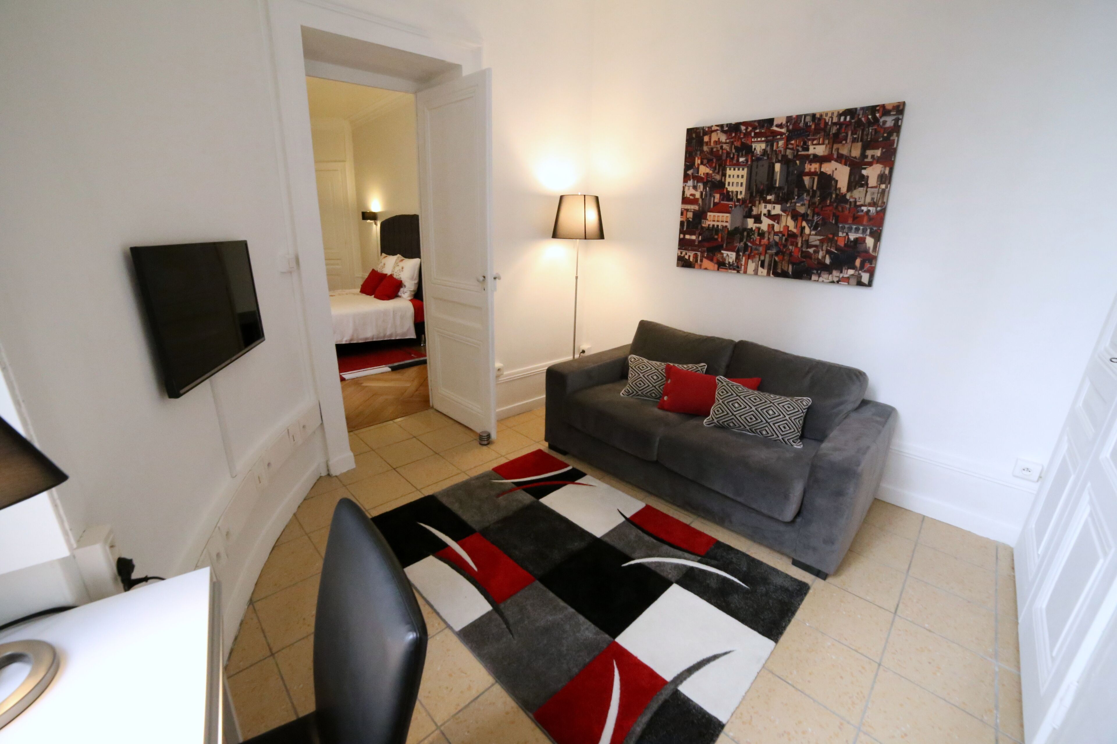 Un salon moderne avec un canapé gris, un tapis noir et rouge, un téléviseur à écran plat et un tableau accroché au mur.