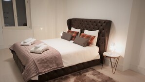 Una cama bien tendida con cabecera marrón, un felpudo mullido y una mesita de noche con lámpara.