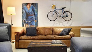 Un salon moderne avec un canapé en cuir marron, une table basse et un tableau représentant une femme à vélo.