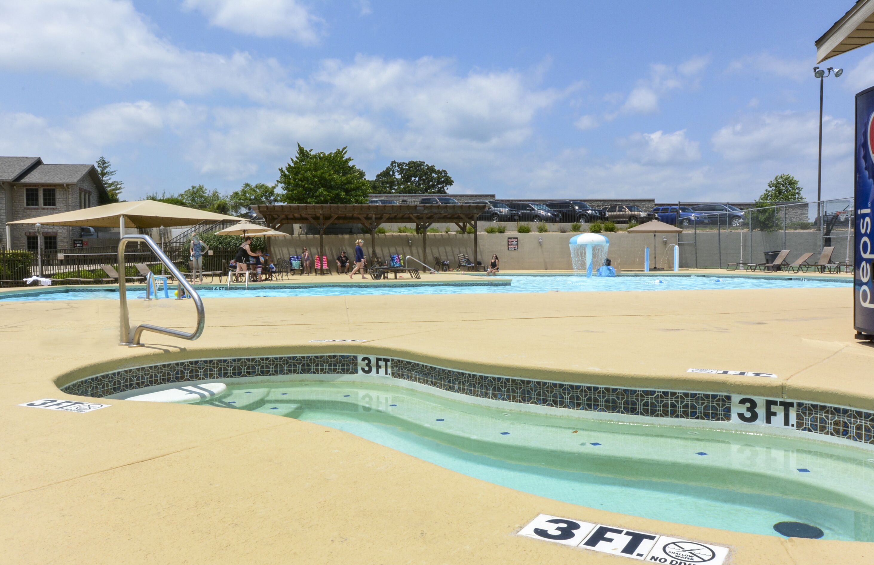 A swimming pool with a 3-foot depth marker, lounge chairs, and umbrellas.