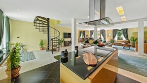 Cocina moderna con una isla central, una escalera de caracol y una sala de estar con sofás y televisión.