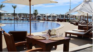 Zona de piscina con sillones de descanso y sombrillas, una mesa con vasos y una botella, y vista al mar.
