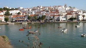Un pueblo costero con edificios blancos y techos rojos, barcos en el agua y un cielo despejado.