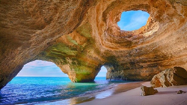 Formación rocosa natural con una abertura circular, una playa de arena y el mar.