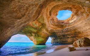 Eine natürliche Felsformation mit einem kreisförmigen Durchbruch, einem Sandstrand und dem Meer.