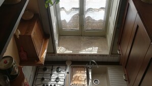 A narrow kitchen with a window, a gas stove, a sink, and a small countertop. - At the gates of Ortigia, apartment in historic building (Siracusa)