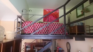 A loft-style bedroom with a bunk bed, a staircase, and a kitchen area in the background. - At the gates of Ortigia, apartment in historic building (Siracusa)