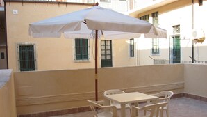 A patio with a table and chairs, a white umbrella, and a building with barred windows. - At the gates of Ortigia, apartment in historic building (Siracusa)