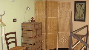 A room with a wooden chair, a lamp, a stack of wicker crates, and a woven partition. - At the gates of Ortigia, apartment in historic building (Siracusa)