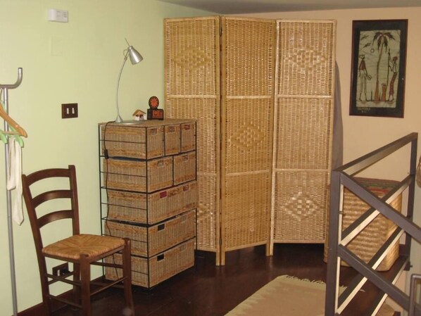 A room with a wooden chair, a lamp, a stack of wicker crates, and a woven partition.
