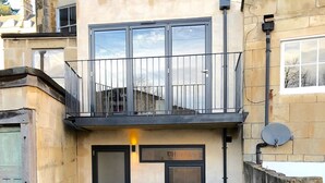 Un edificio con fachada de piedra, un balcón con barandilla de metal y un patio empedrado.