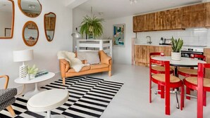 Una sala de estar moderna con un sofá, una mesa de comedor con sillas rojas y una cocina con armarios de madera y encimera blanca.