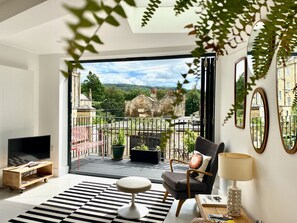 A modern living room with a large TV, a comfortable chair, a small table, and a view of a cityscape through a glass door.