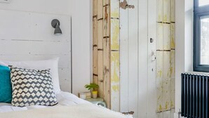 Un dormitorio con cama, mesita de noche, lámpara, radiador y ventana.