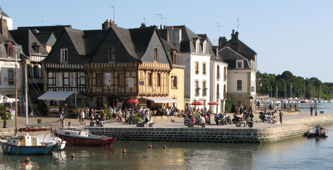 A waterfront promenade with historic buildings, a dock with boats, and people enjoying the area.