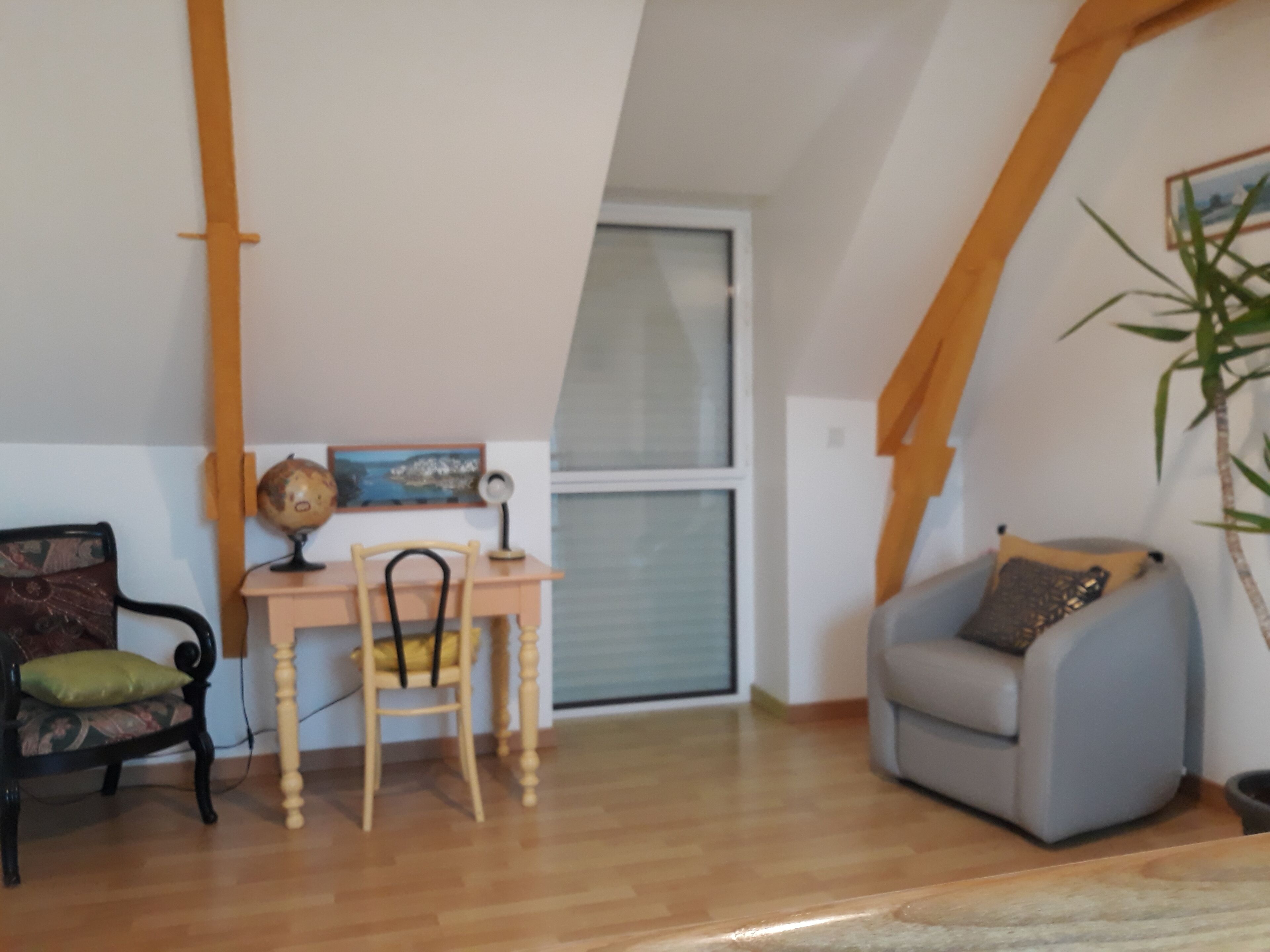 Une pièce comprenant un bureau en bois, une chaise, un globe terrestre, un tableau encadré, une fenêtre et une plante.