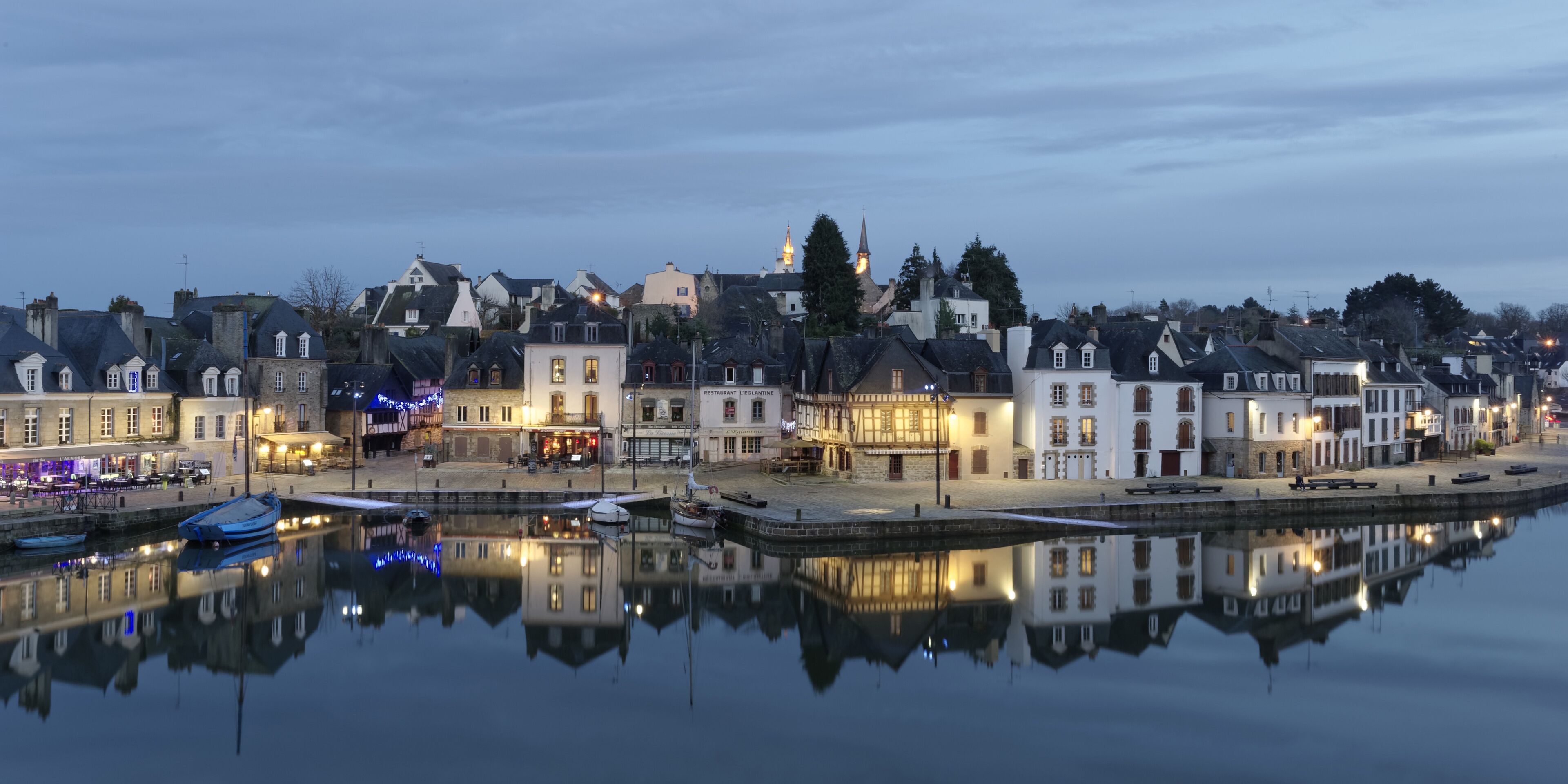 A waterfront town with historic buildings, a calm river, and boats docked.
