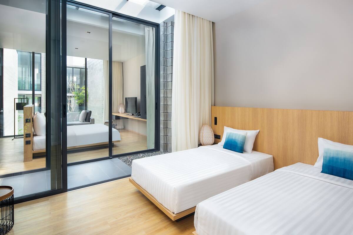 A modern hotel room with two beds, a large sliding glass door leading to a balcony, and a wooden headboard.