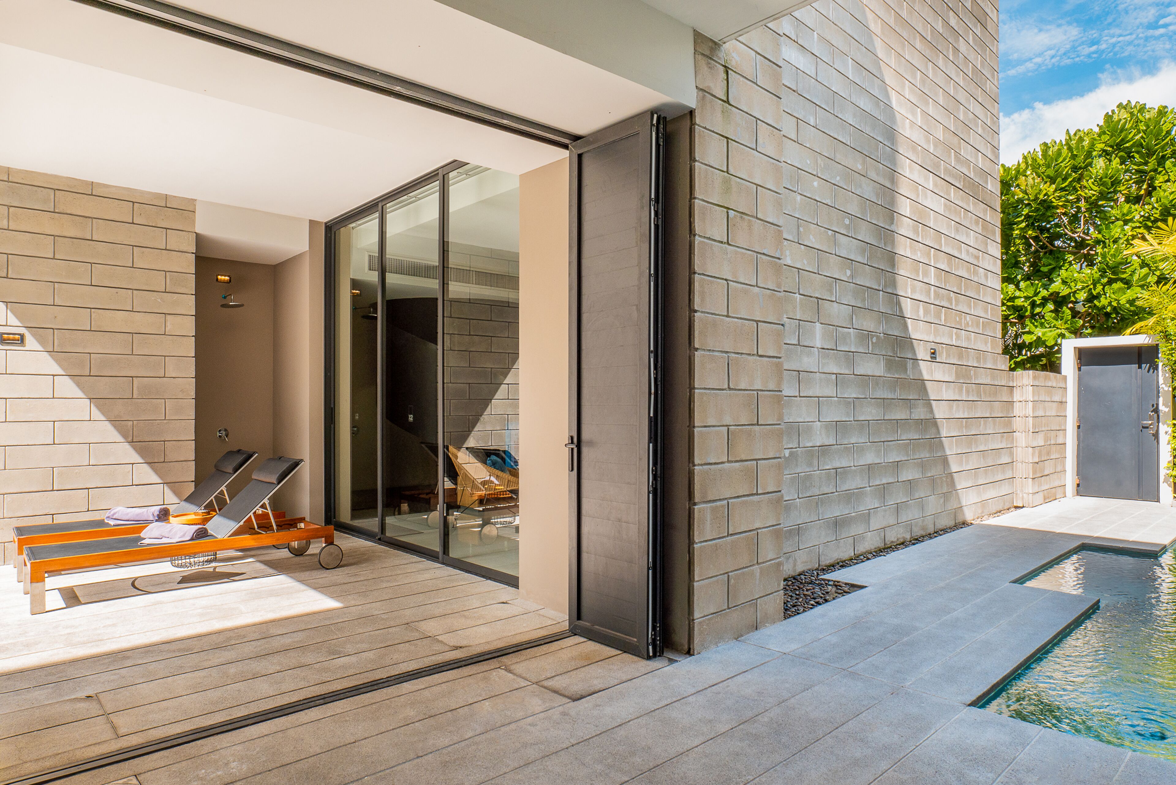 Un espacio exterior moderno con piscina, sillones de descanso y un ventanal que da a un área techada.