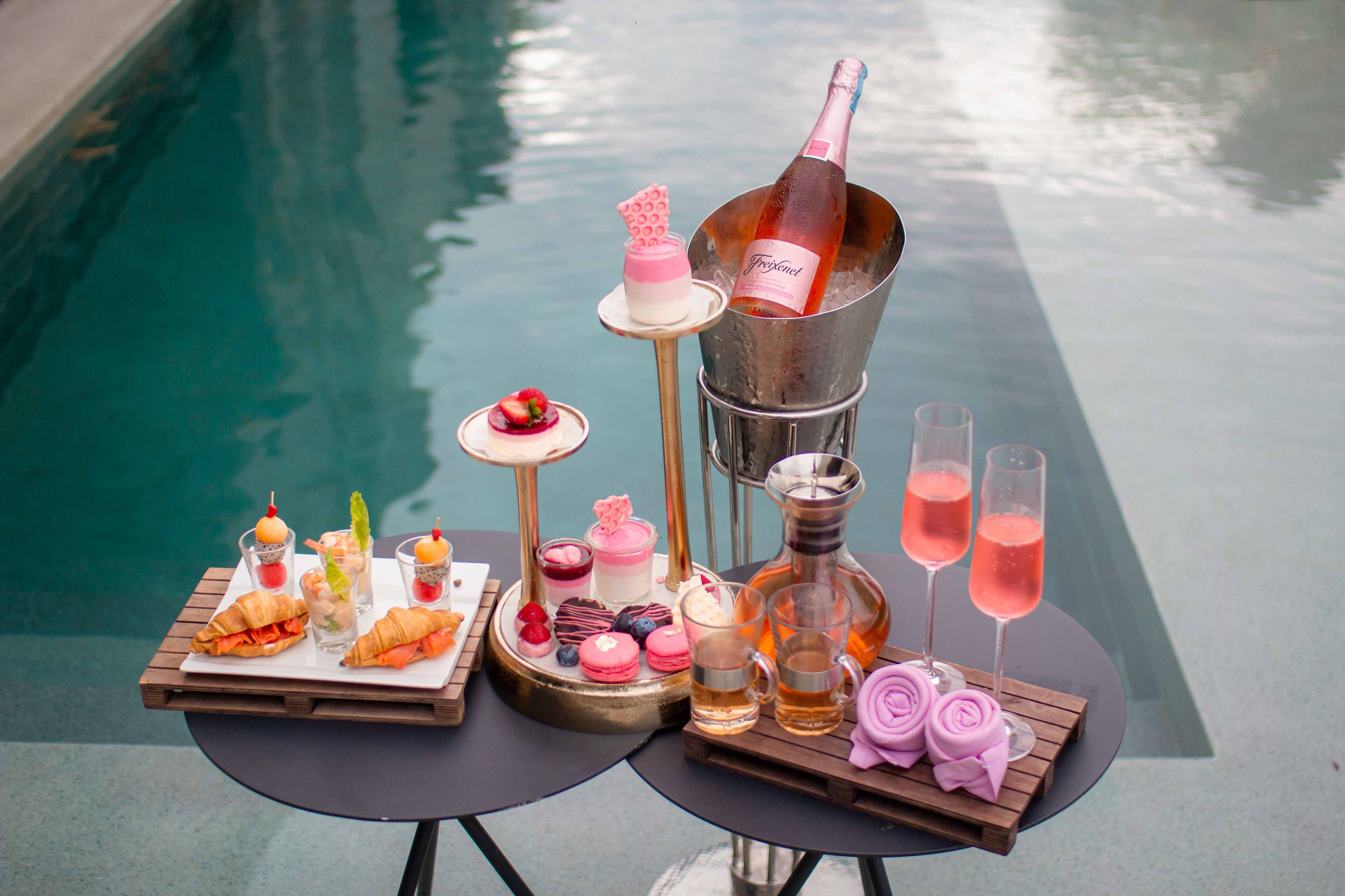 Two tables with food and drinks by a pool.